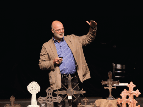 White man in blue shirt and jacket in front of crosses