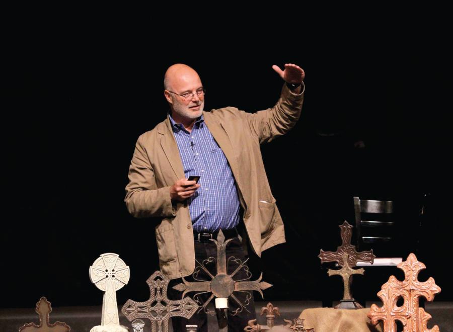 White man in blue shirt and jacket in front of crosses