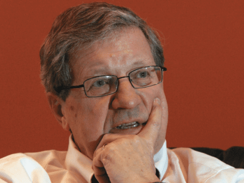 White man in glasses and white dress shirt against orange background
