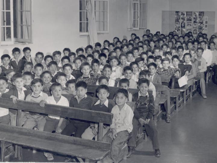 Black and white photo of young Indigenous boys in many rows in auditorium