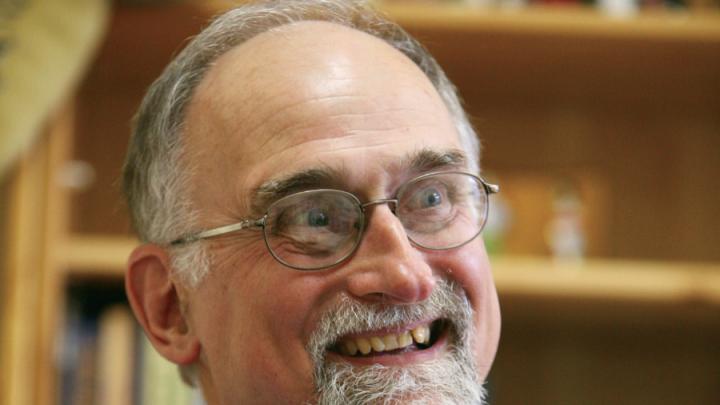 Grey-haired white man in beard, glasses and suit is smiling