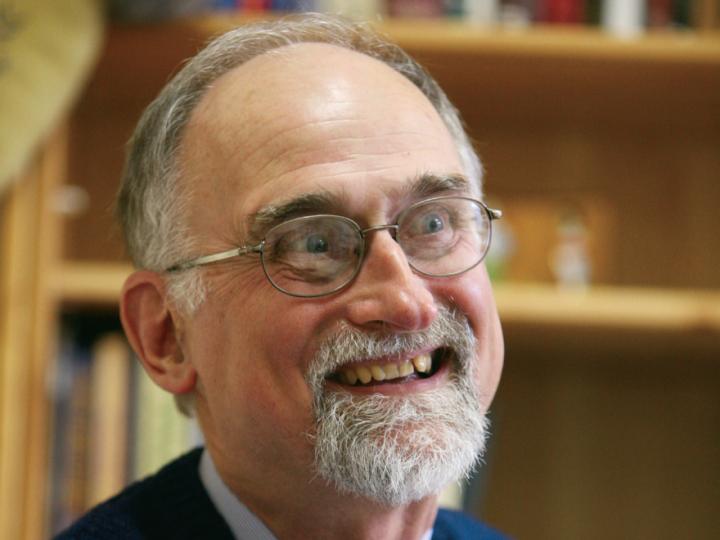 Grey-haired white man in beard, glasses and suit is smiling