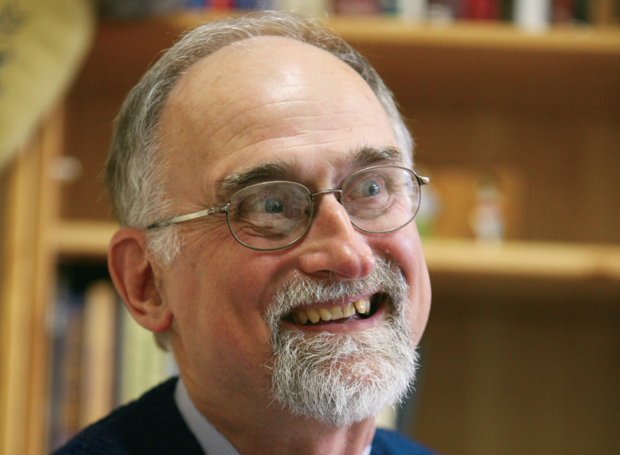 Grey-haired white man in beard, glasses and suit is smiling