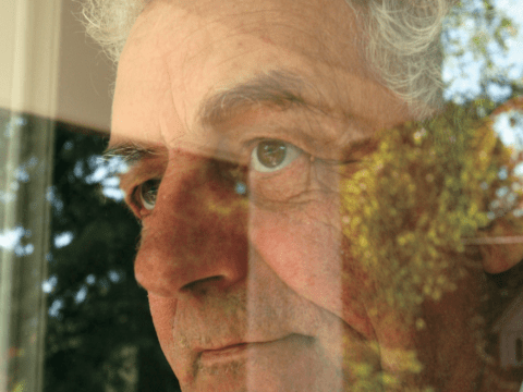 Partial view of white-haired white man looking through window