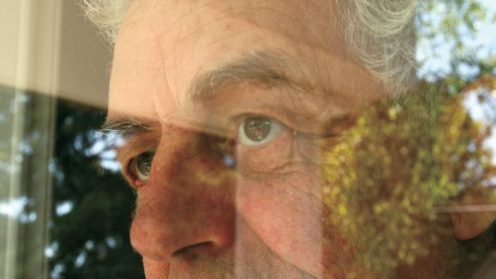 Partial view of white-haired white man looking through window