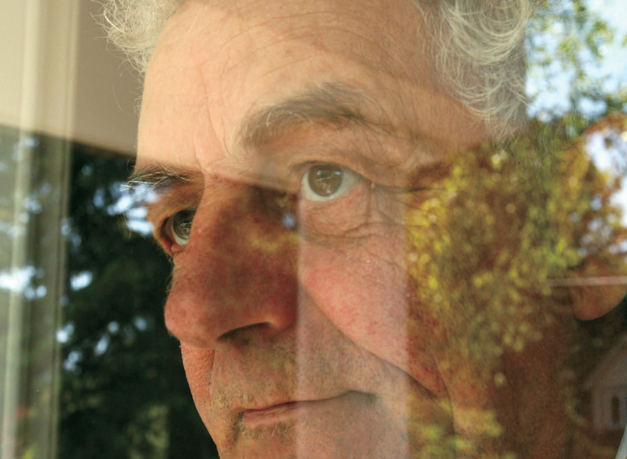 Partial view of white-haired white man looking through window