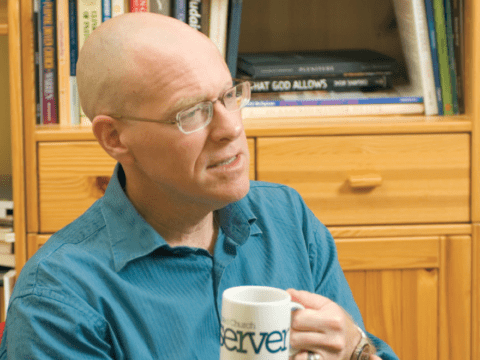 Bald white man in blue shirt holding coffee cup