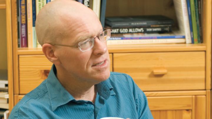 Bald white man in blue shirt holding coffee cup