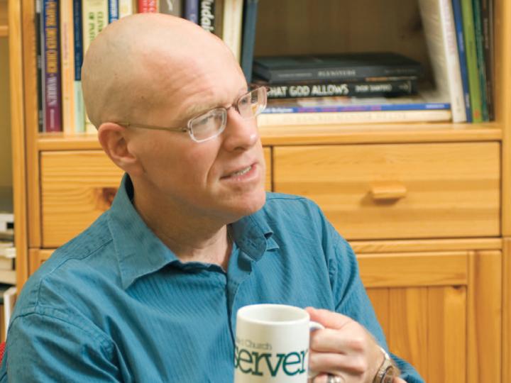 Bald white man in blue shirt holding coffee cup