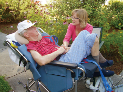 Old white man in wheelchair and his daughter holding his hand