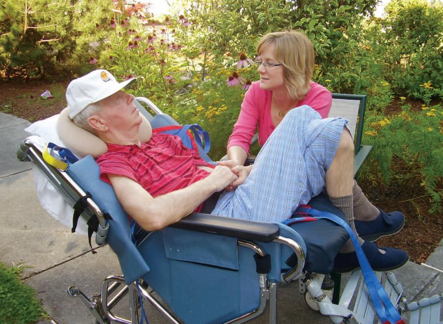 Old white man in wheelchair and his daughter holding his hand