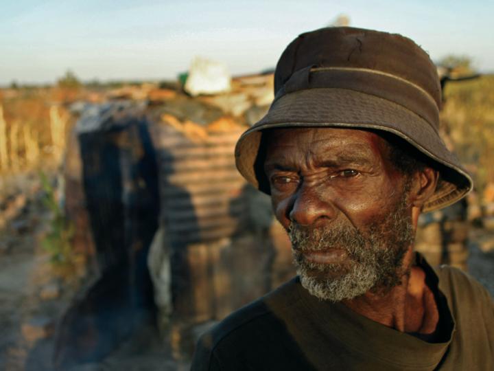 Elderly Black man in hat against African backdrop