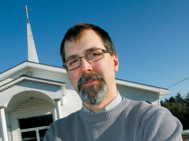 White man with beard and glasses against blue sky and church