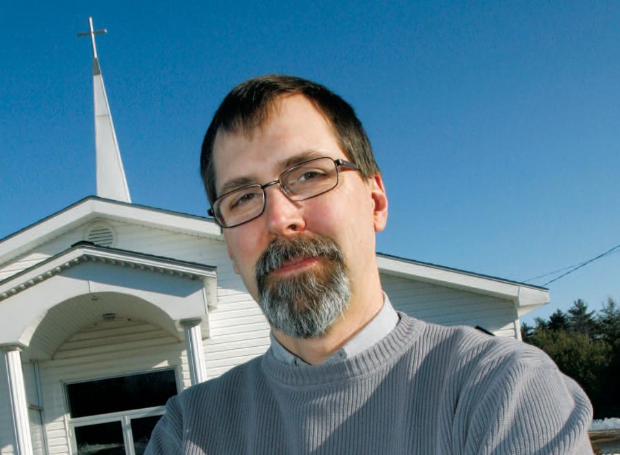 White man with beard and glasses against blue sky and church