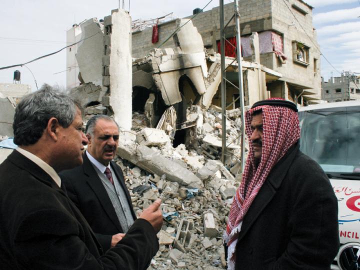 Three men stand before the ruins of a building in Gaza
