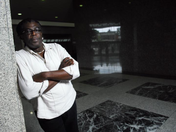 Black man in white shirt with arms crossed leaning against wall