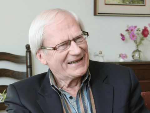 White-haired white man with glasses wearing striped shirt and dark jacket