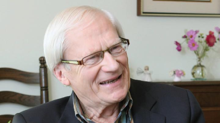 White-haired white man with glasses wearing striped shirt and dark jacket