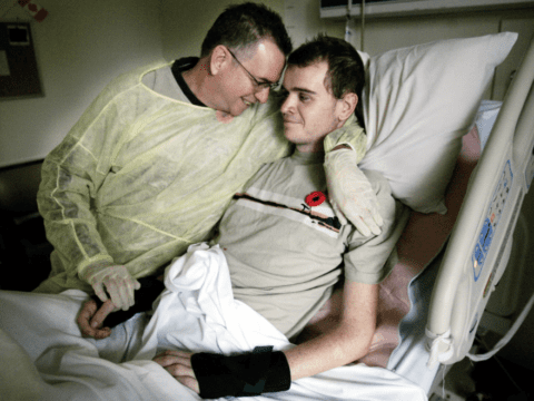 Father cradling adult son in hospital bed