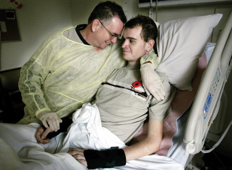 Father cradling adult son in hospital bed