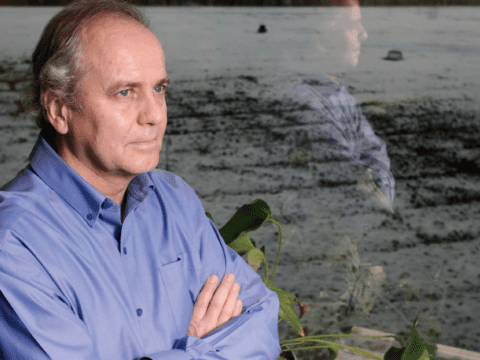 White man in blue shirt standing with arms crossed