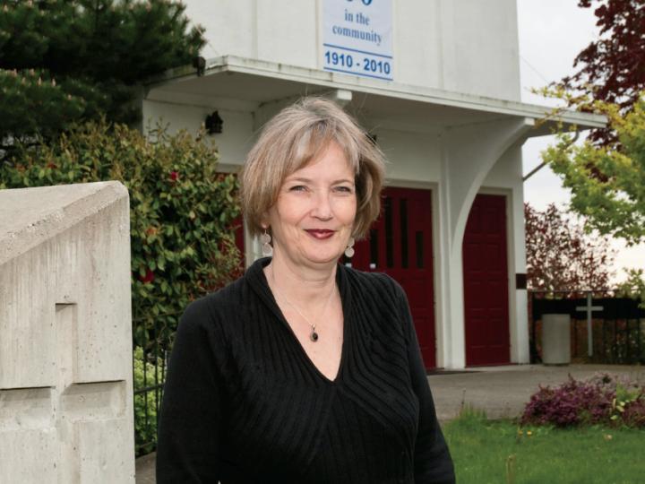 White woman in black top standing in front of a church
