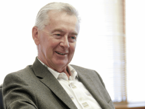 White-haired white man in suit jacket and open-necked white shirt