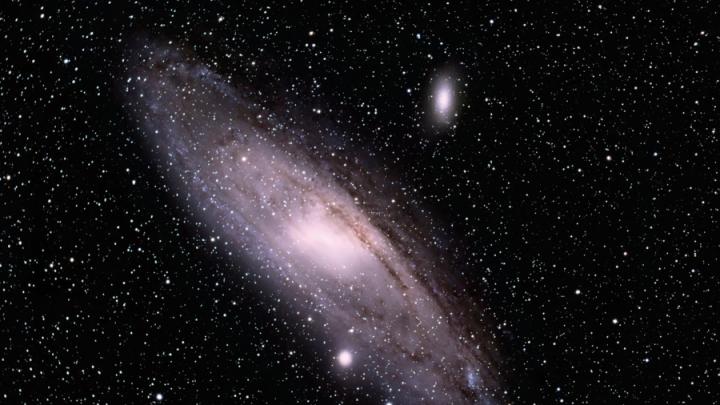 Photograph of Andromeda Galaxy with the stars of the universe in the background. The galaxy's many solar systems form a circular shape giving the impression that Andromeda is a shining whole in an endless field of the universe's mysterious vastness.