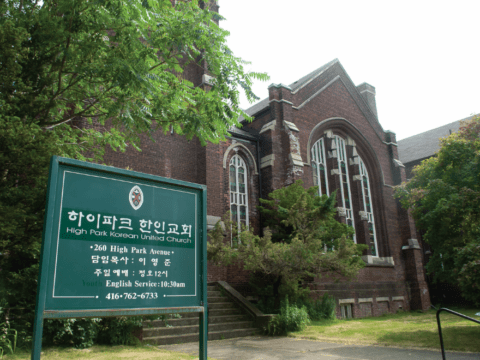 United Church in Toronto neighbourhood with green sign and trees in front.