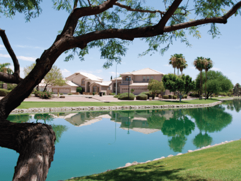 Landscape of monster home with lake in Tempe, Arizona. The lake is still, giving a near perfect reflection of the house