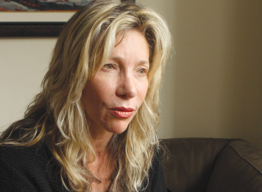 White woman with blonde medium layered cut hair and hazel eyes staring into the distance. She has no smile.