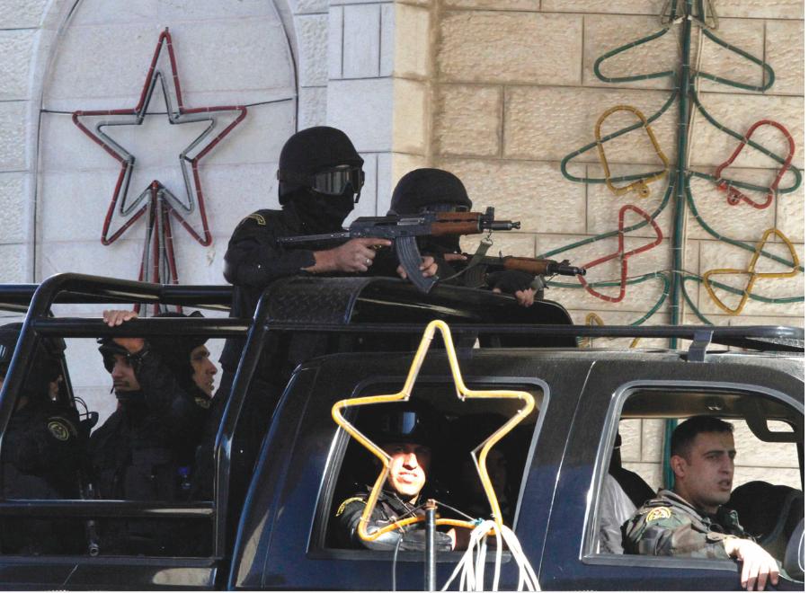 A vehicle carrying armed soldiers pass in front of a wall partially covered with Christmas decorations. The armed soldiers are carrying what seems like Kalashnikovs