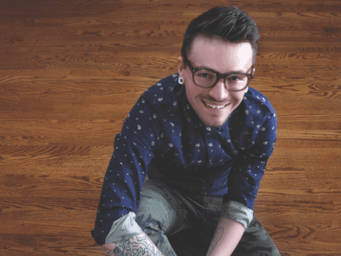 Young white man sitting on wooden floor looking up into camera