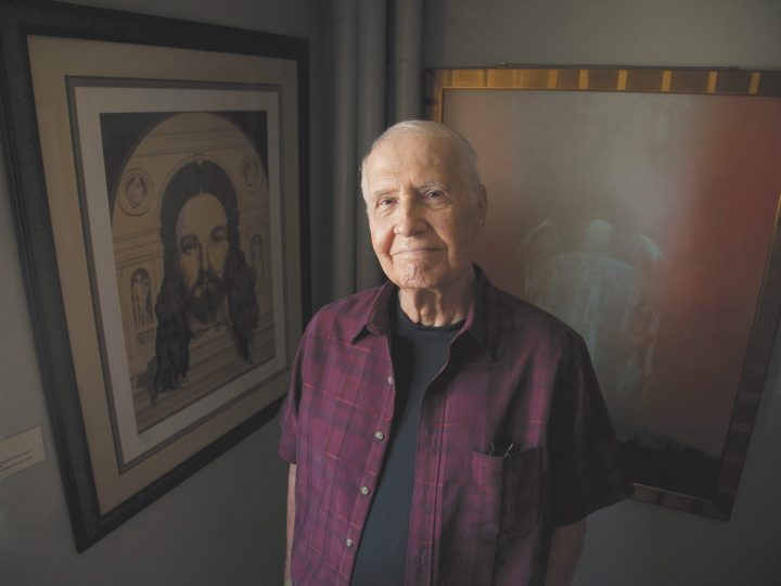 older man looks at camera, painting of Jesus behind him