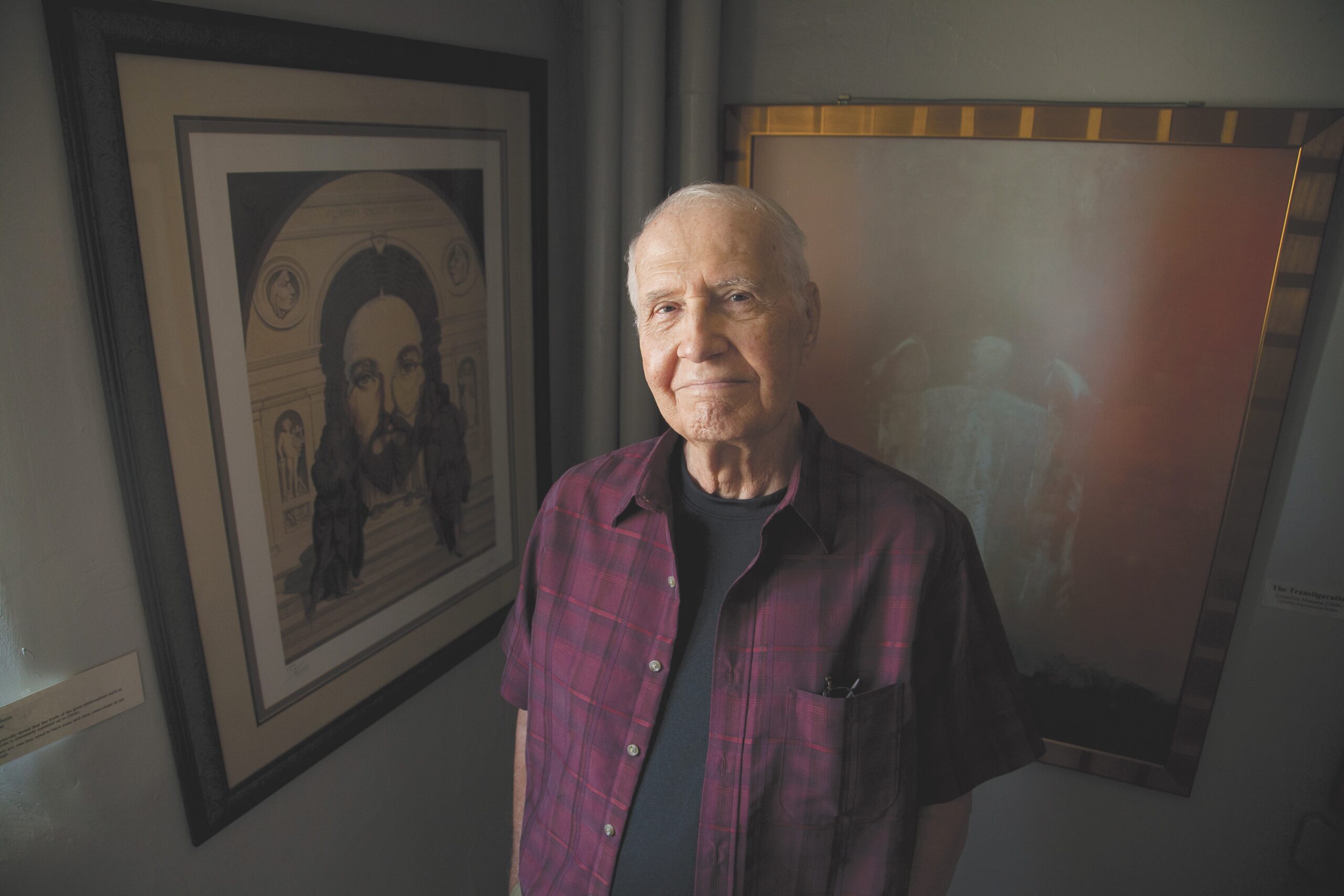 older man looks at camera, painting of Jesus behind him