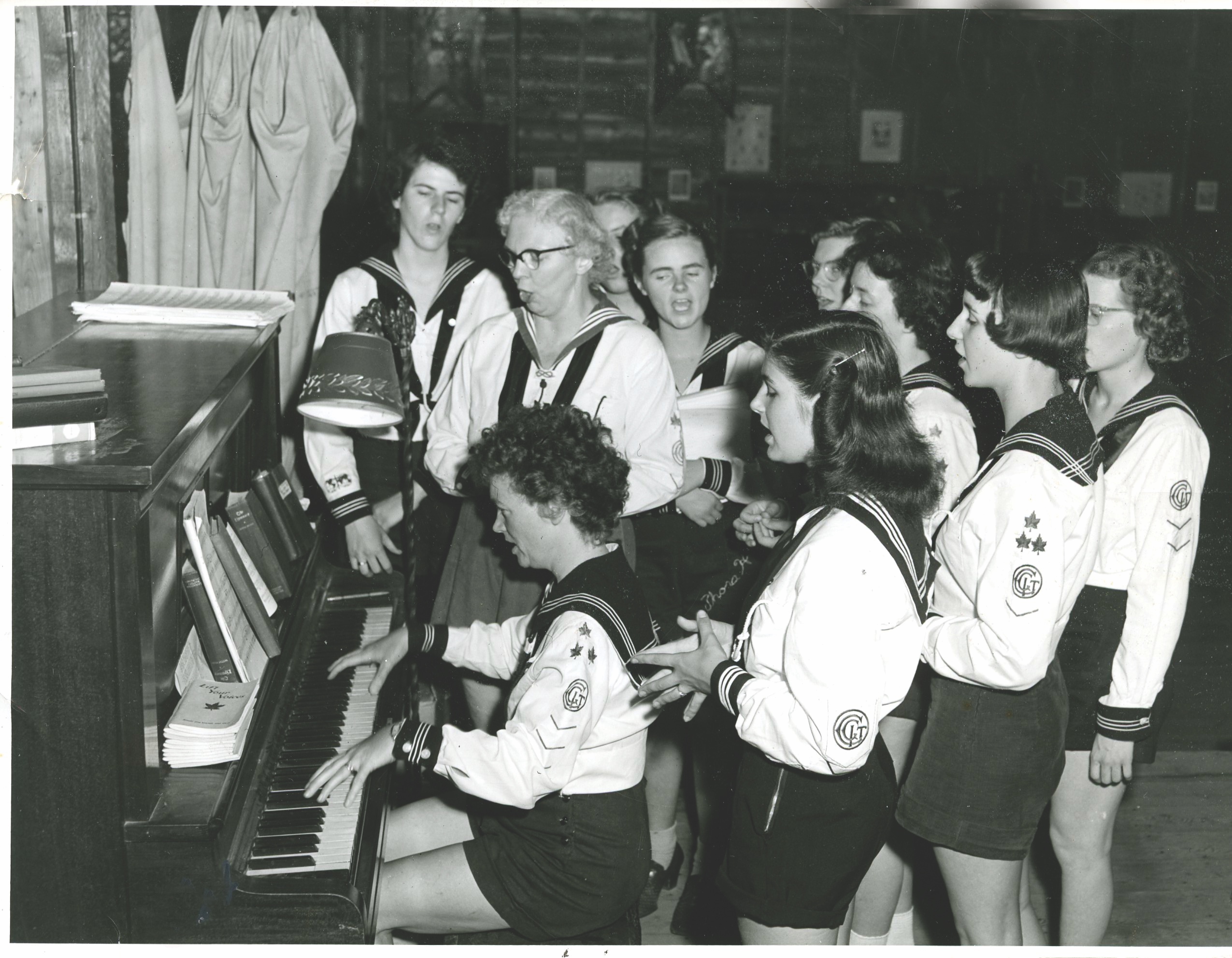 Archival photo of young women singing around piano