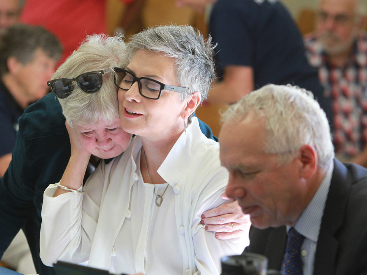 Atheist minister Gretta Vosper receives a hug from Fran Ota, also a United Church minister, before the start of the Toronto Conference sub-Executive meeting, held on Sept. 15. Vosper’s lawyer, Julian Falconer, sits to her left. Photo by Hugh Wesley