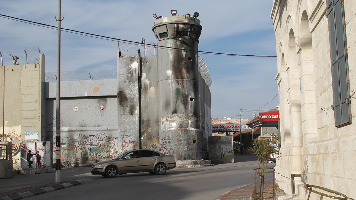 A sooty watchtower, part of the wall separating Bethlehem from Jerusalem, looms over Hebron Road in the West Bank. Photo Byron Rempel-Burkholder