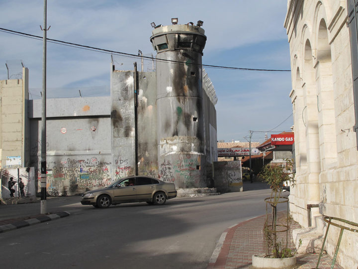 A sooty watchtower, part of the wall separating Bethlehem from Jerusalem, looms over Hebron Road in the West Bank. Photo Byron Rempel-Burkholder