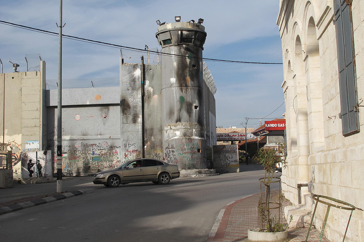 A sooty watchtower, part of the wall separating Bethlehem from Jerusalem, looms over Hebron Road in the West Bank. Photo Byron Rempel-Burkholder