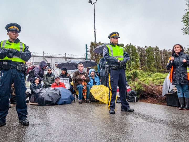 Song leader, police and gate blockers in front of the Kinder Morgan gates. Photo by Kimiko Karpoff