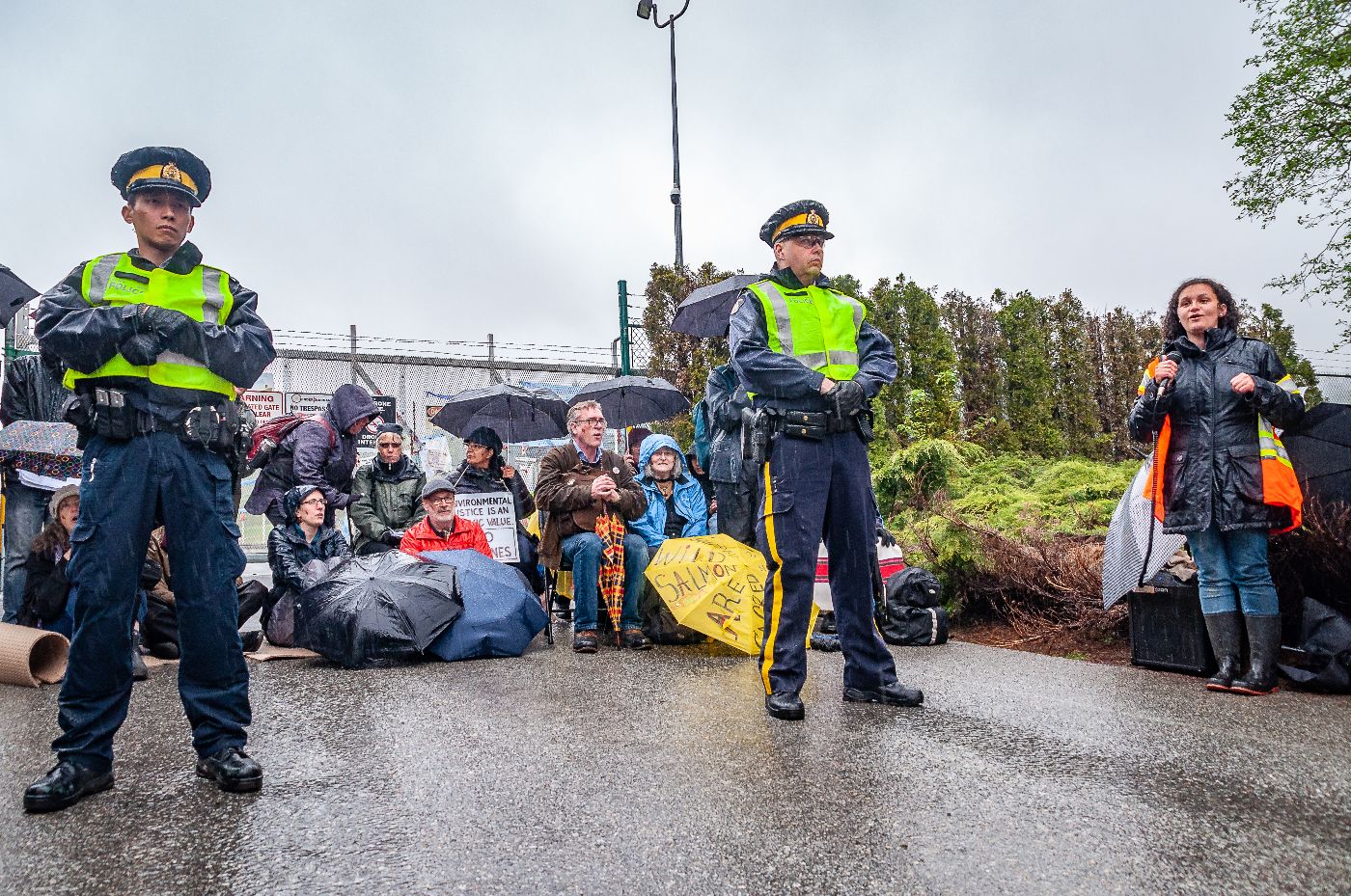 Song leader, police and gate blockers in front of the Kinder Morgan gates. Photo by Kimiko Karpoff