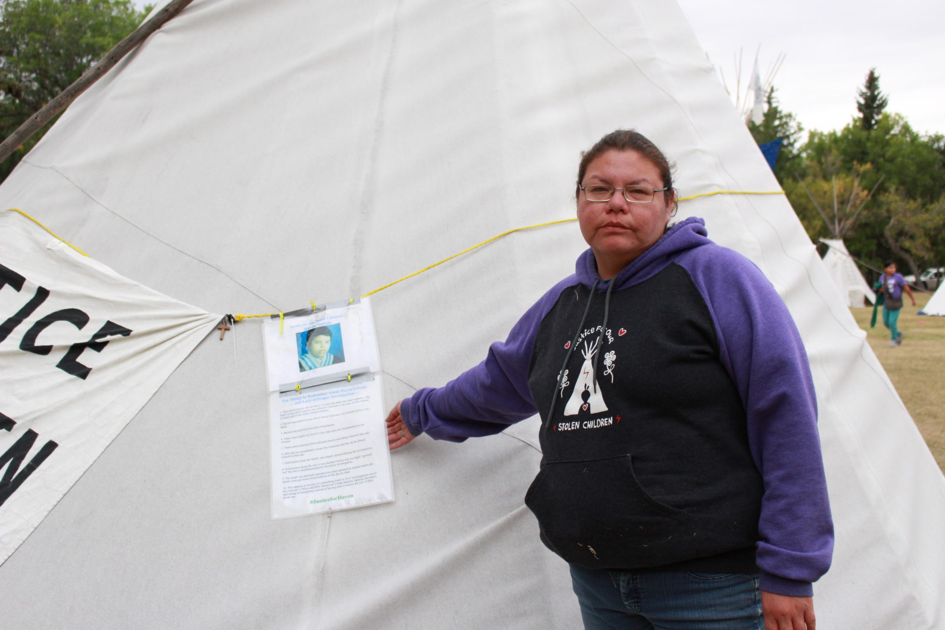 Richelle Dubois stands beside a sign discussing the issues in the police investigation into the death of her son, Haven, at the Justice for Our Stolen Children protest camp in Regina, Sask., on Sept. 2, 2018. (Photo: Alexa Lawlor)