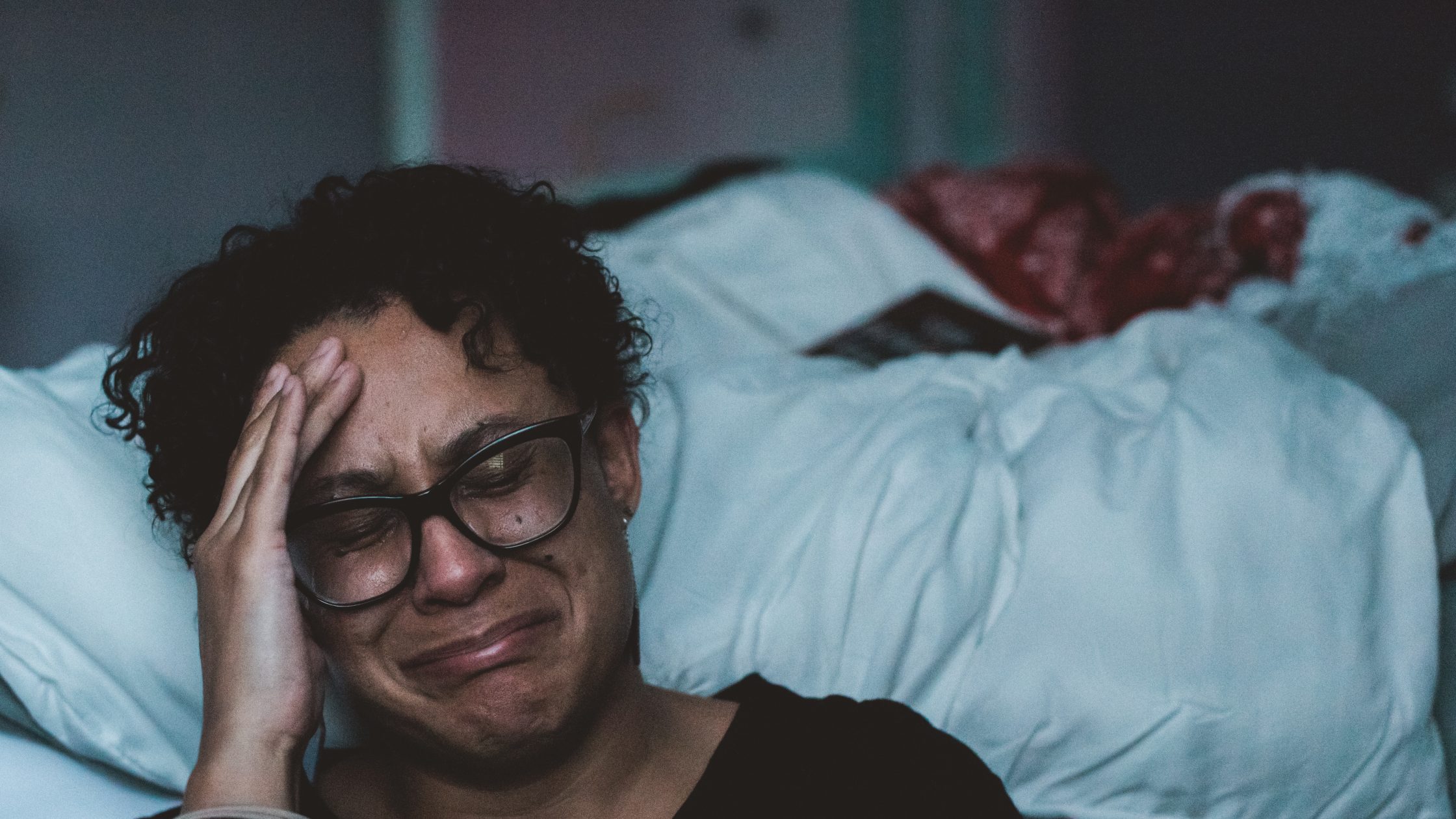 A sad woman cries next to a bed. (Photo: Claudia/Unsplash)