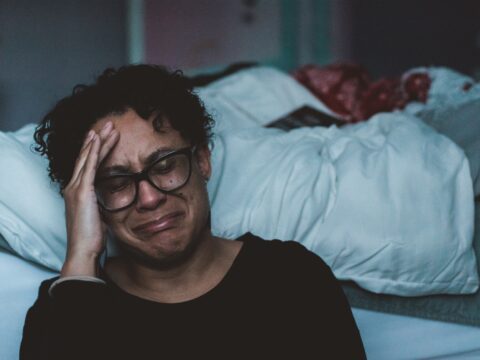 A sad woman cries next to a bed. (Photo: Claudia/Unsplash)