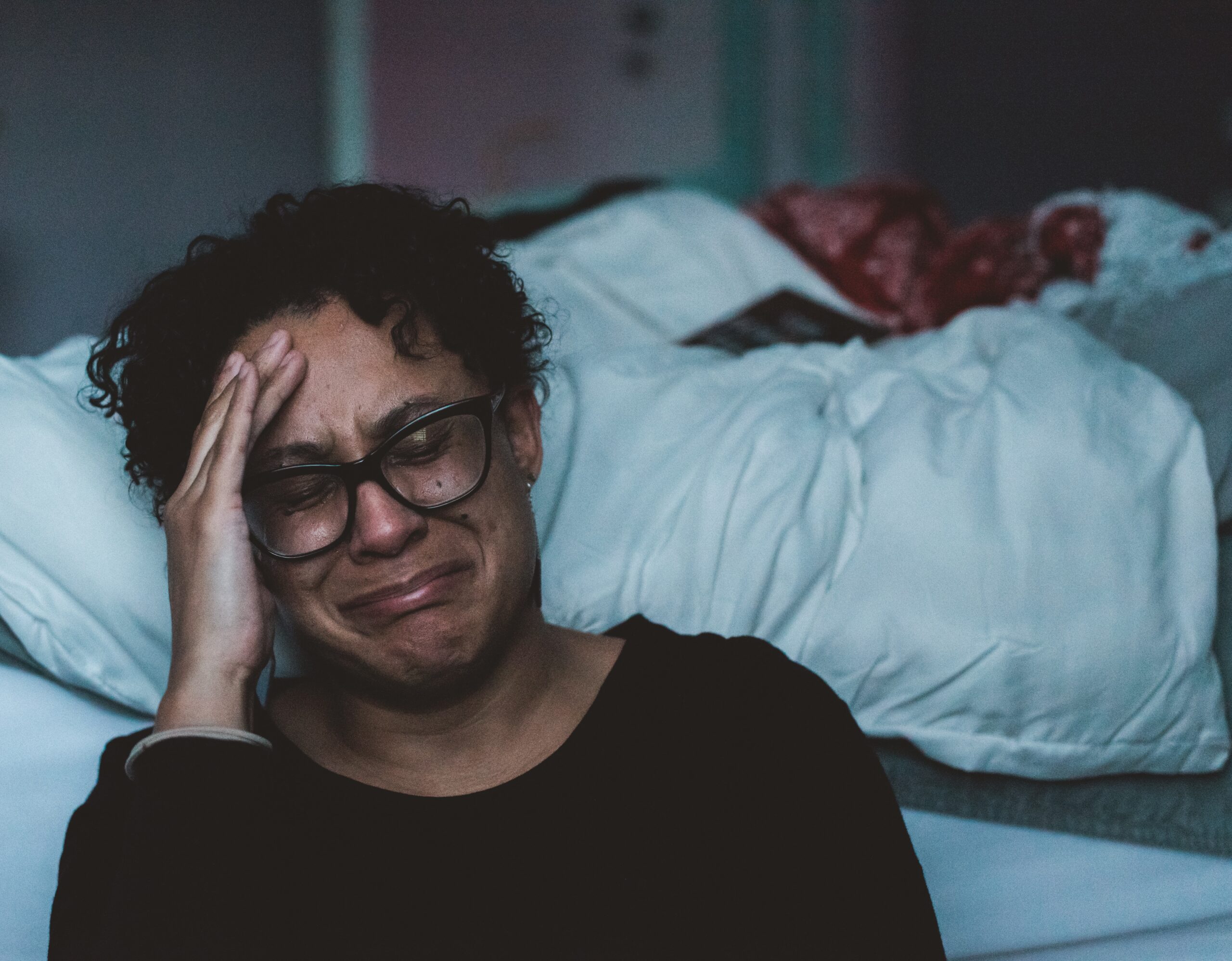 A sad woman cries next to a bed. (Photo: Claudia/Unsplash)