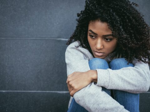 An upset woman sits, huddled.