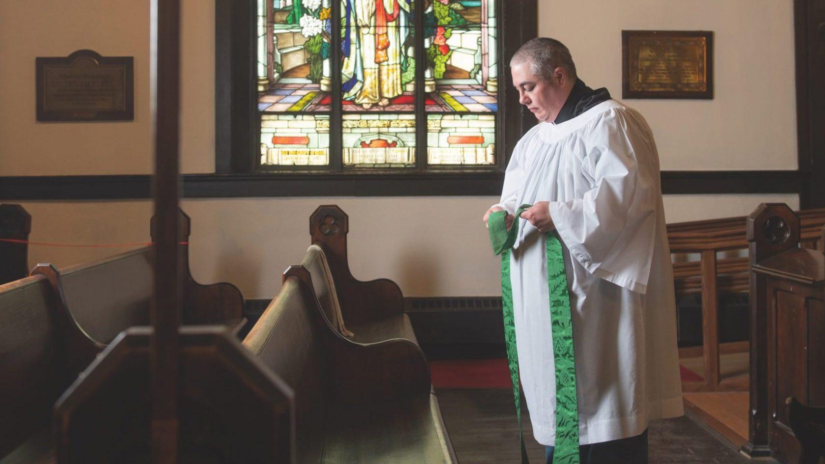 Anglican priest Theo Robinson stands in front of a church pew.