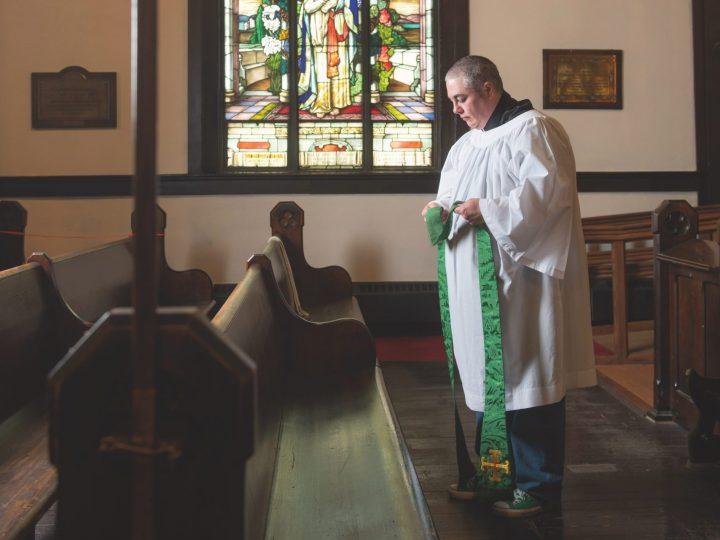 Anglican priest Theo Robinson stands in front of a church pew.