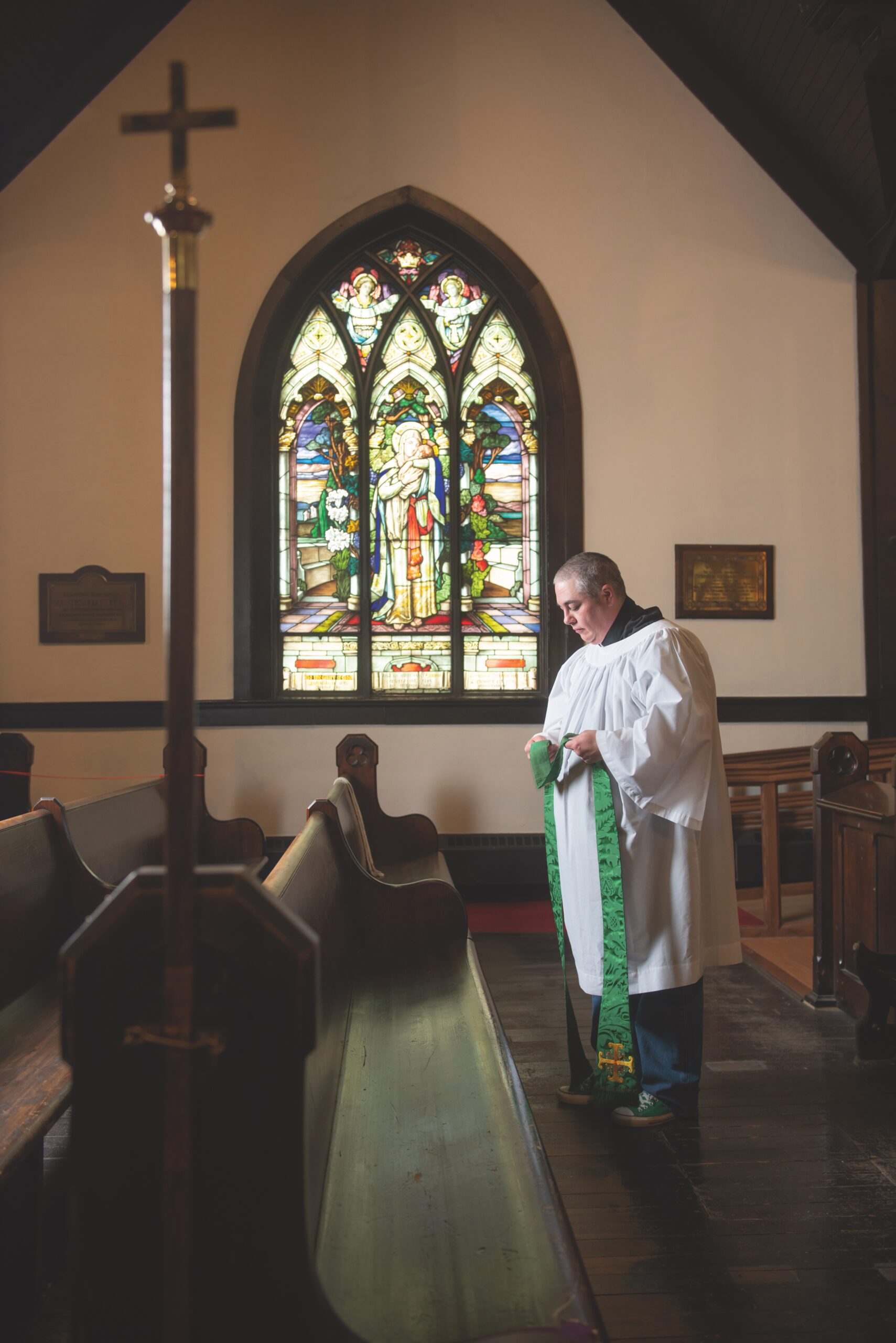 Anglican priest Theo Robinson stands in front of a church pew.